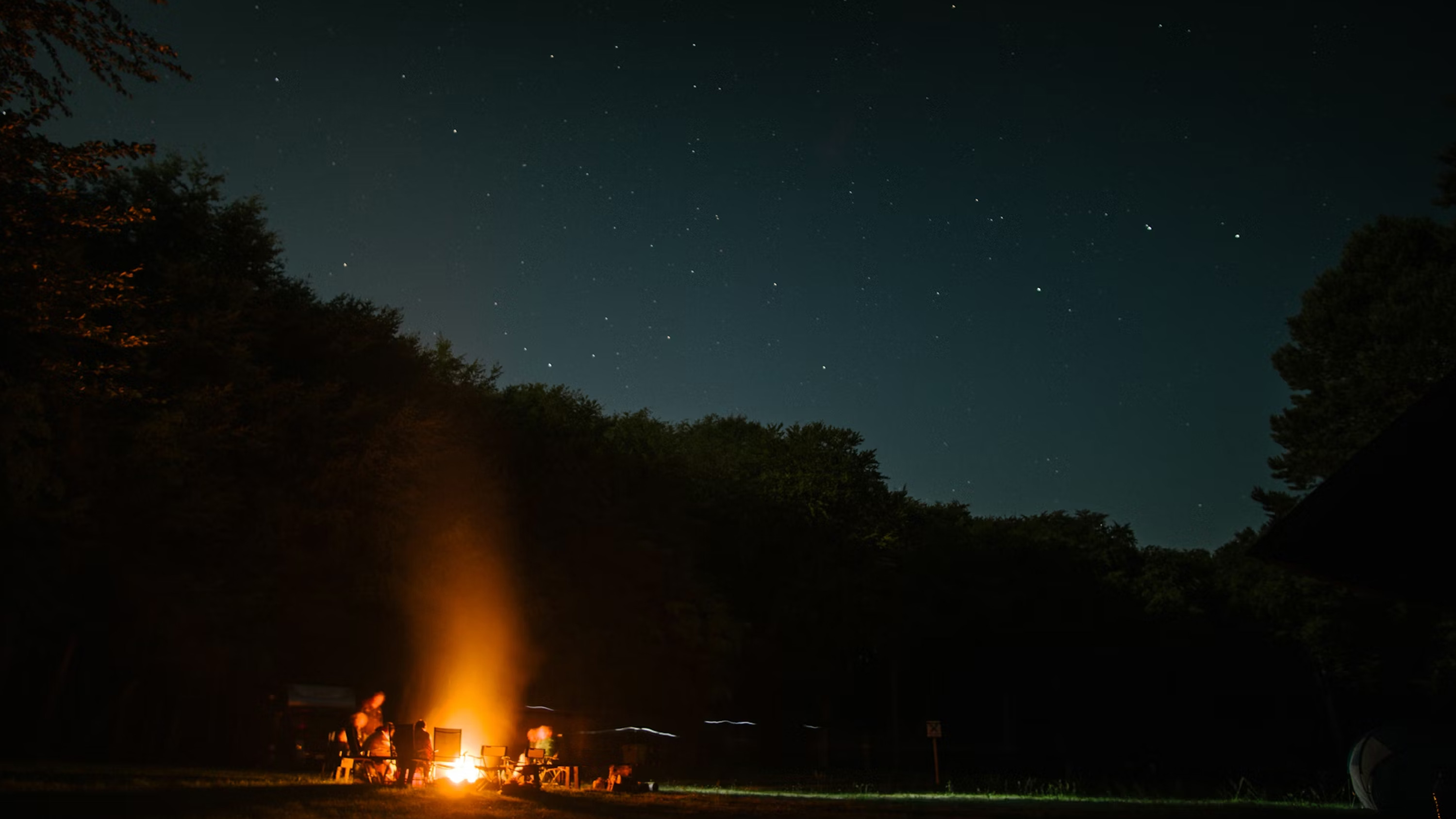 Fire pit blazing by a tent campsite with mountains in the background.