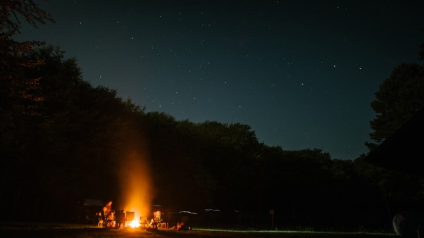 Fire pit blazing by a tent campsite with mountains in the background.