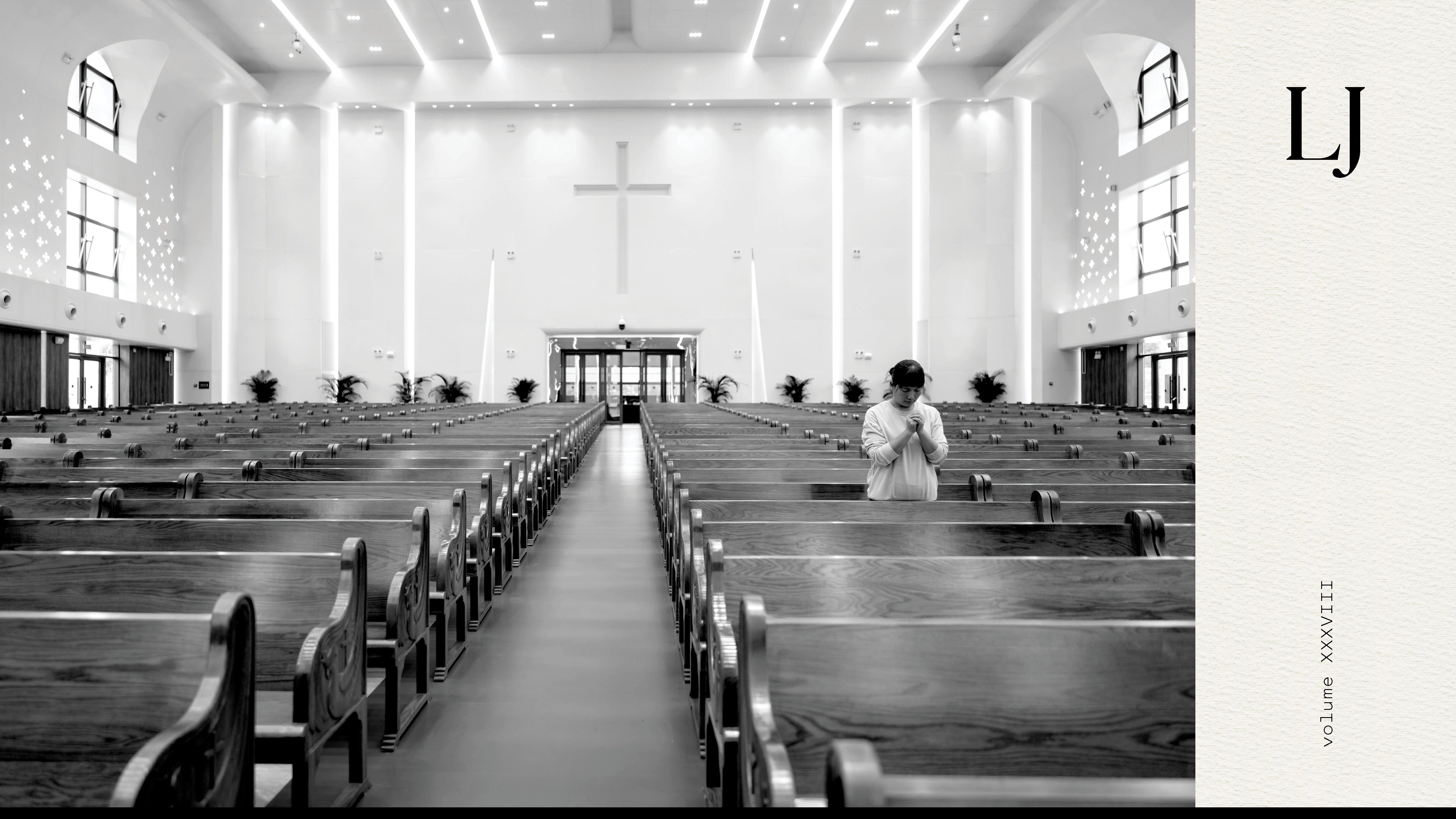 Black and white photo of a church with many empty pews and only one person standing and praying
