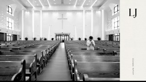 Black and white photo of a church with many empty pews and only one person standing and praying