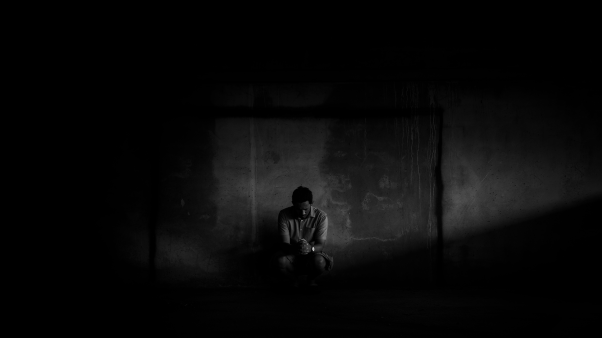 man alone praying in a dark room