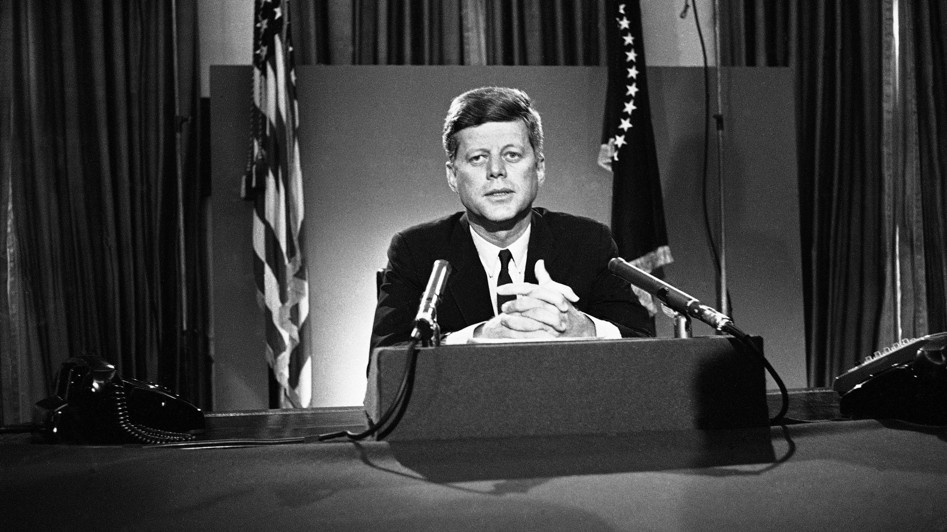 President John F. Kennedy sits behind microphones at his desk in Washington after finishing his radio-television broadcast to the nation on the nuclear test ban agreement initialed by negotiators in Moscow.