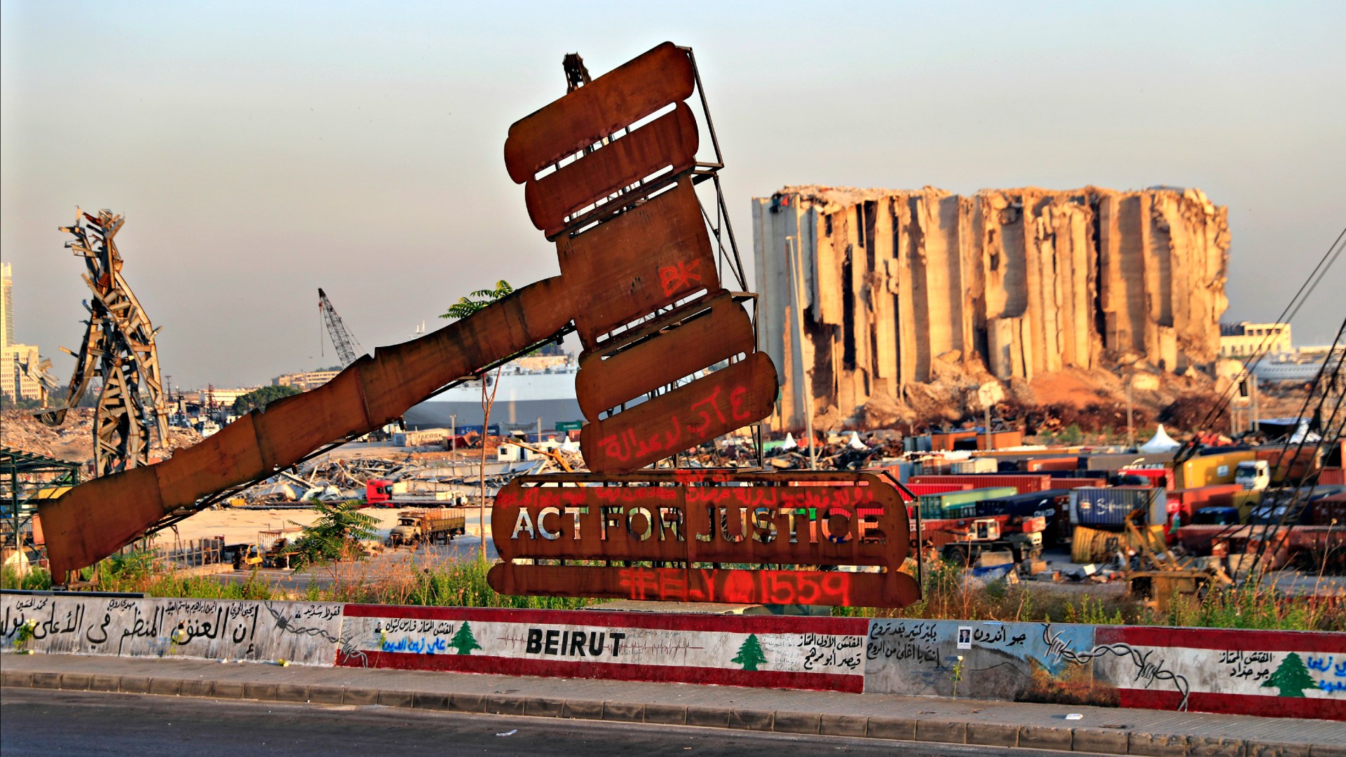 A justice symbol monument is seen August 4, 2021, in front of towering grain silos that were gutted in the massive August 2020 explosion at the port of Beirut that claimed the lives of more than 200 people in Lebanon.