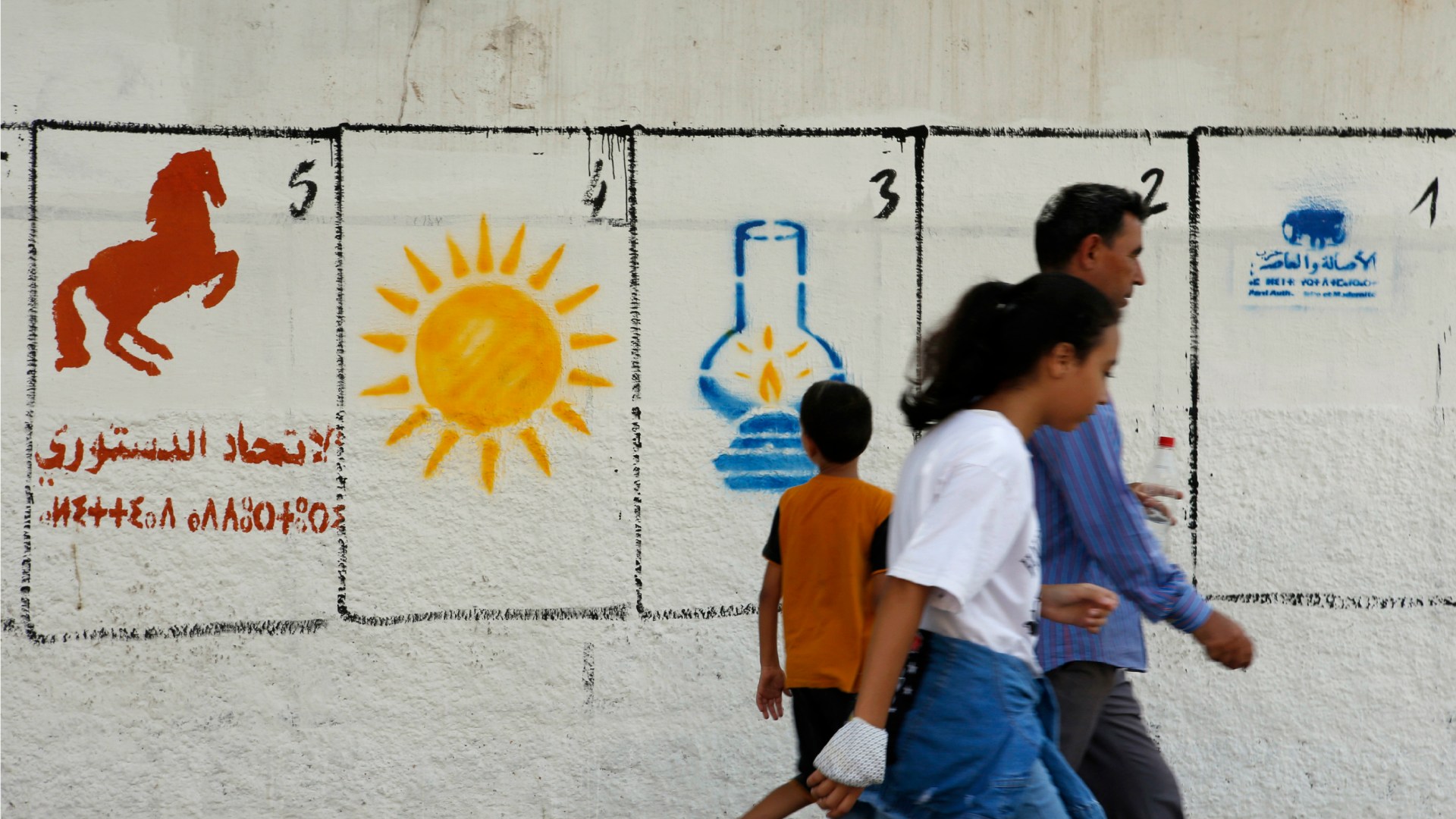 A Moroccan family walk past electoral paintings representing political party logos for the Sept. 8 municipal elections in Casablanca.