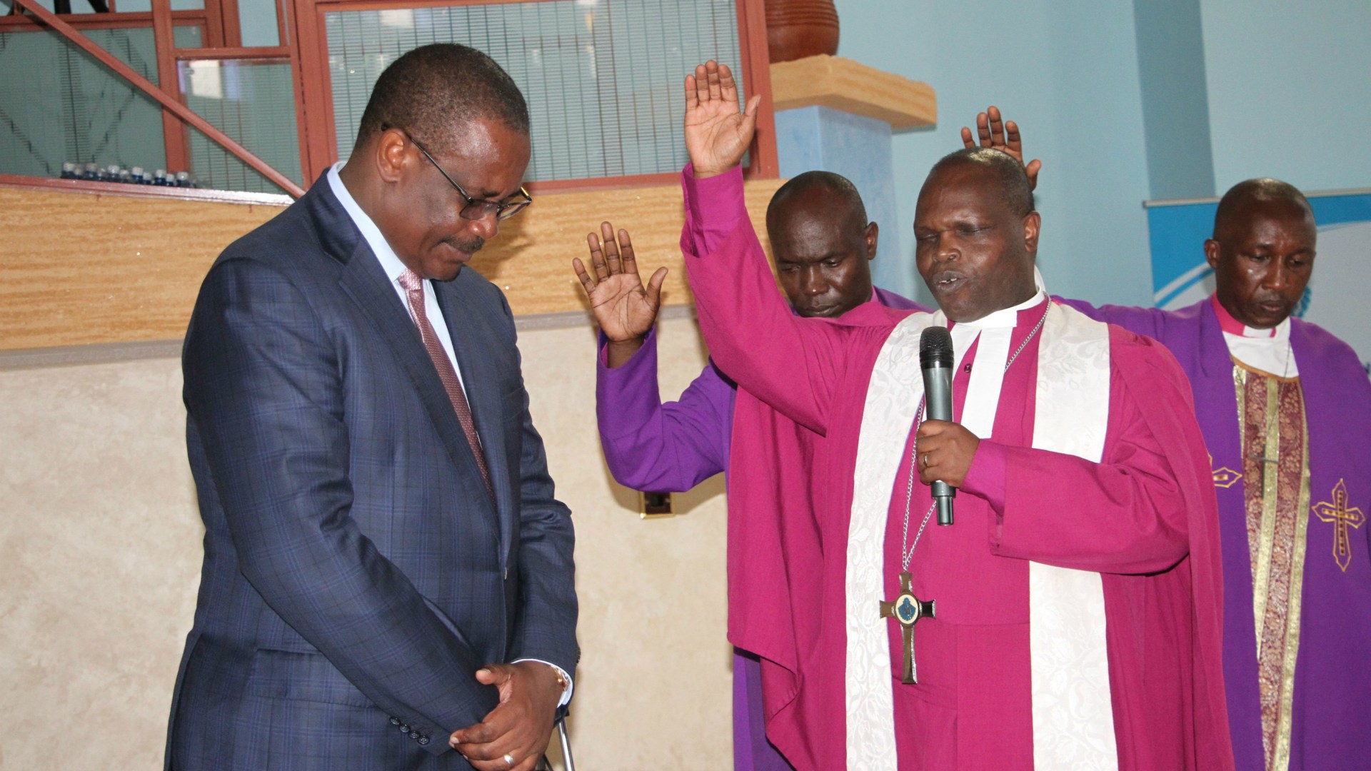 Holding a microphone, Joseph Ntombura, presiding bishop of the Methodist Church in Kenya, prays over former Nairobi Governor Evans Kidero (left) in November 2015.