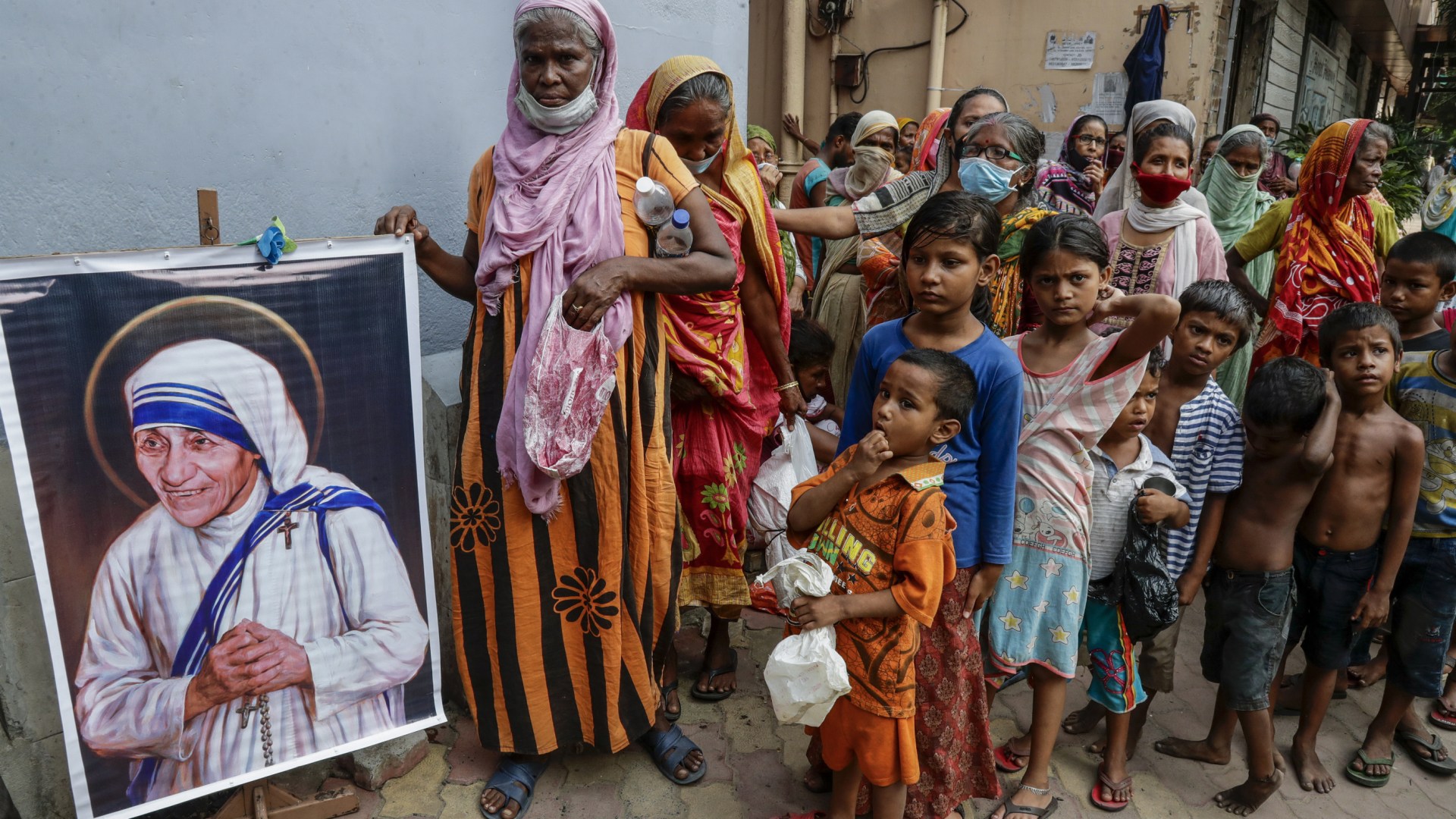 Homeless people gather beside a portrait of Mother Teresa, founder of the Missionaries of Charity, to collect free food outside the order's headquarters in Kolkata, India, on August 26, 2021.