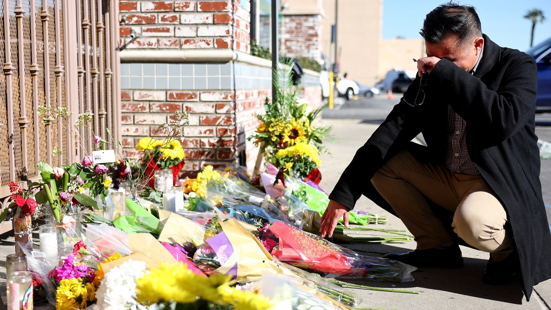 A man kneels at a makeshift memorial outside the scene of a deadly mass shooting at a ballroom dance studio in Monterey Park, California.