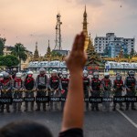 A protester makes a three-finger salute in front of a row of riot police, who are holding roses given to them by protesters.