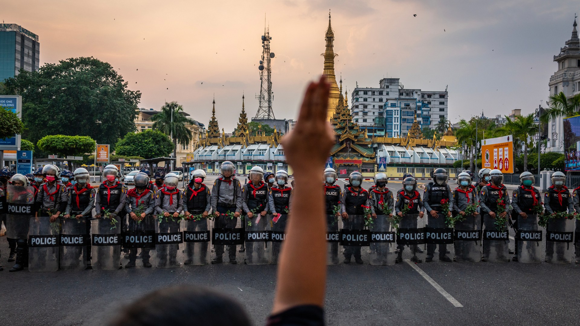 A protester makes a three-finger salute in front of a row of riot police, who are holding roses given to them by protesters.