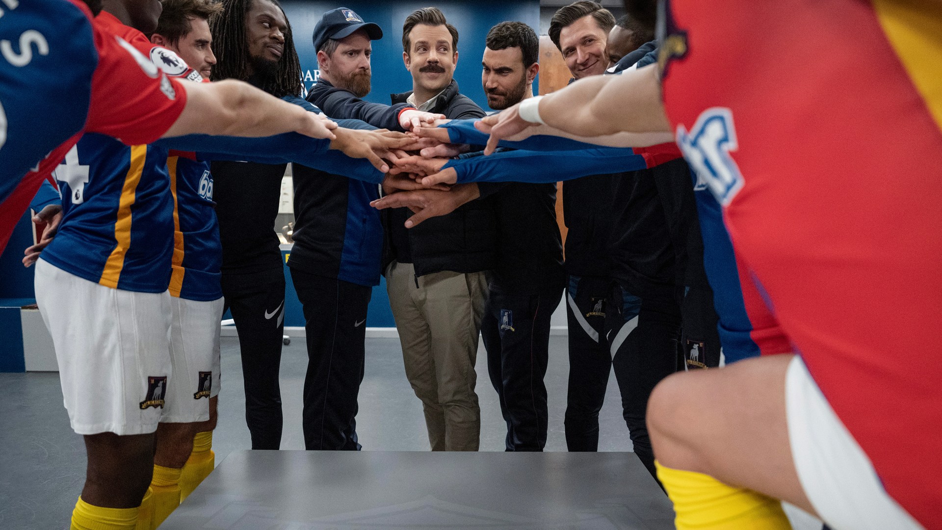 Ted Lasso and the AFC Richmond soccer players in a team huddle.