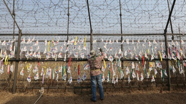 A man hangs a national flag wishing for the reunification and peace of the two Koreas on the wire fence in South Korea near the border of North Korea.