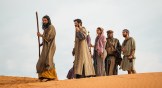 Wasim No’mani as Moses holding a staff in the desert with Israelites walking behind him