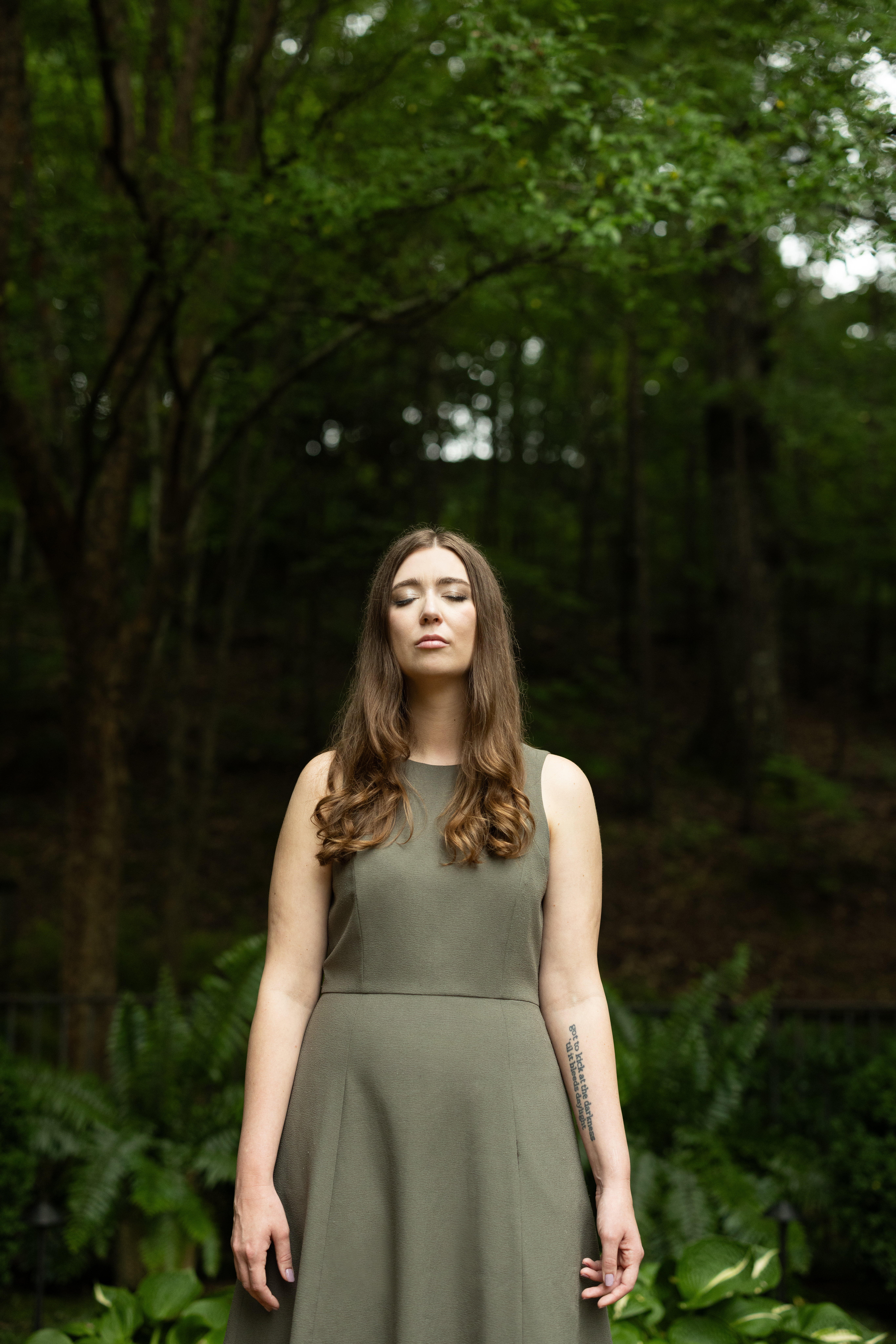 portrait of Lindsay Holifield standing in a forrest with her eyes closed