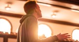 A student worshiping at the Asbury Revival with a bright light shining through a window near his heart.