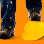 A construction workers dirty jeans and boots with one boot standing on a yellow construction hat