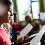 Girl holds sheet music with kids singing.