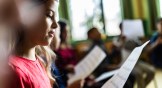 Girl holds sheet music with kids singing.