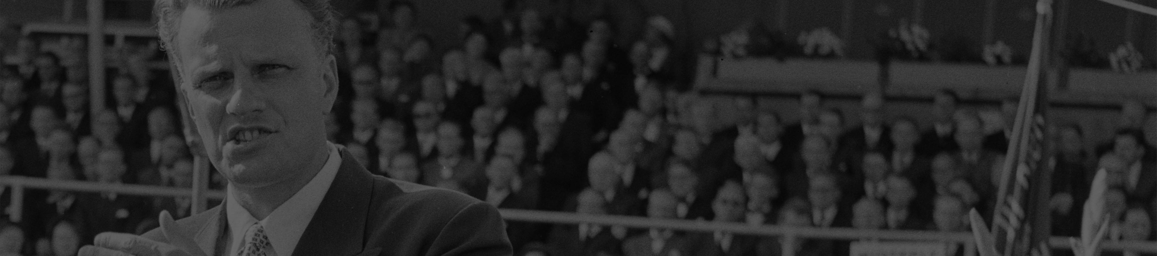 A photo of Billy Graham speaking with a crowd behind him