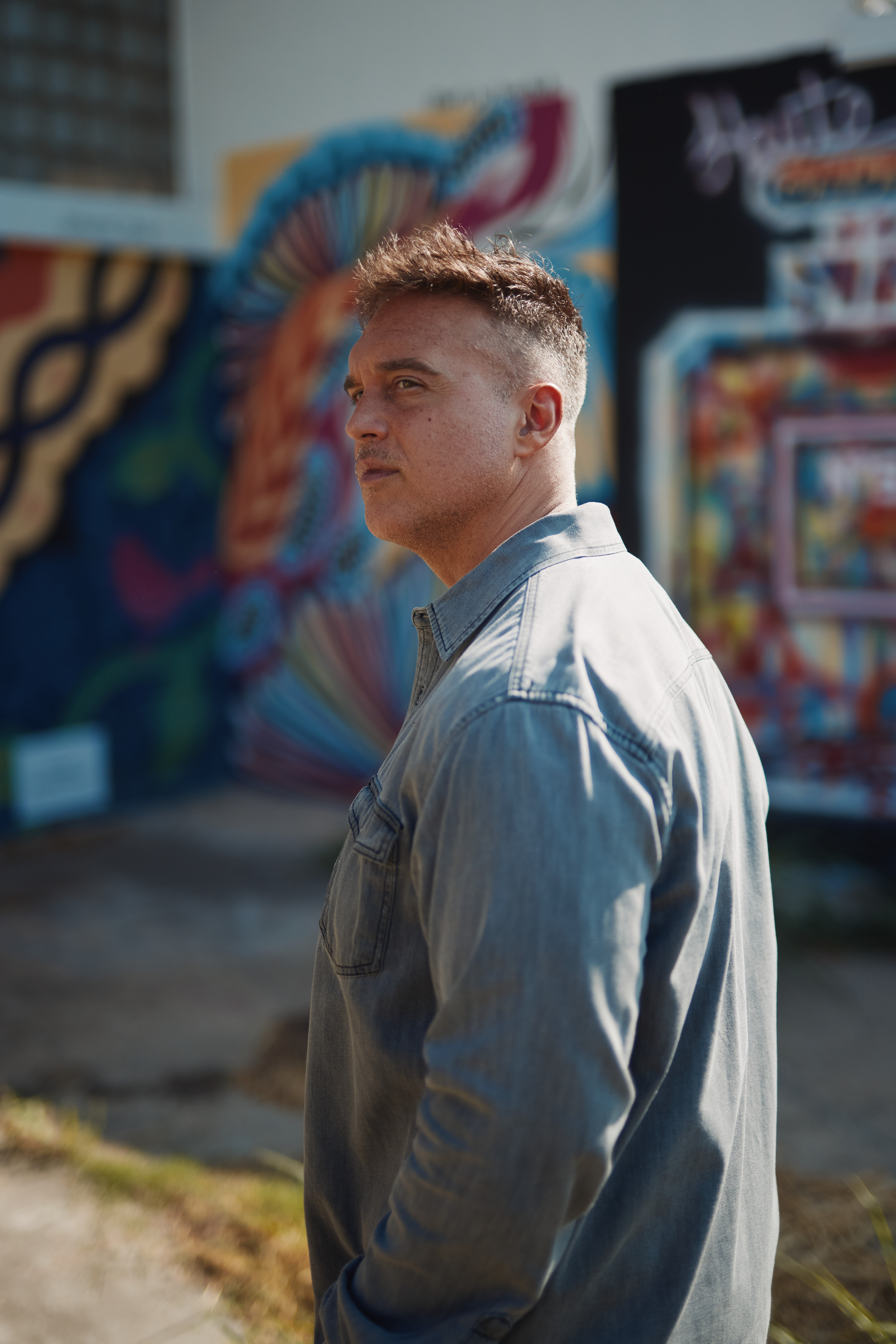Portrait of Joshua Broome standing against a graffitied wall