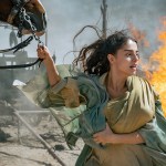 Mary holding onto a horse with a fire behind her.