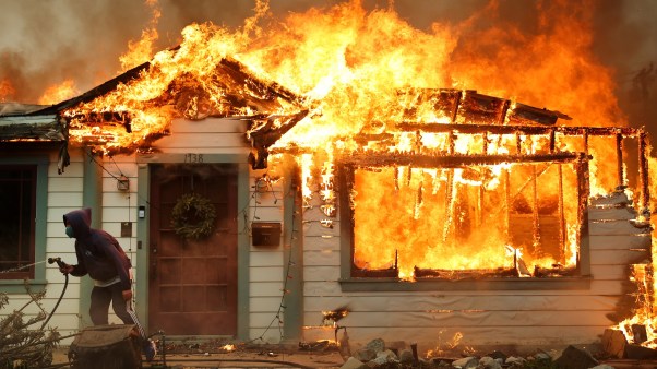A person uses a garden hose in an effort to save a neighboring home from catching fire during the Eaton Fire on January 8, 2025 in Altadena, California.