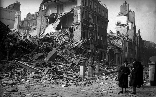 Two women stand amid debris from bomb damage during World War II