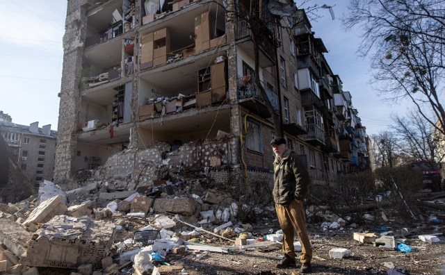A Ukrainian man stands amid debris in front of a residential apartment complex that was heavily damaged by a Russian attack.