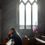 A man prays in a UK church amid bad news about the future of seminary education.
