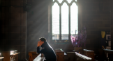 A man prays in a UK church amid bad news about the future of seminary education.