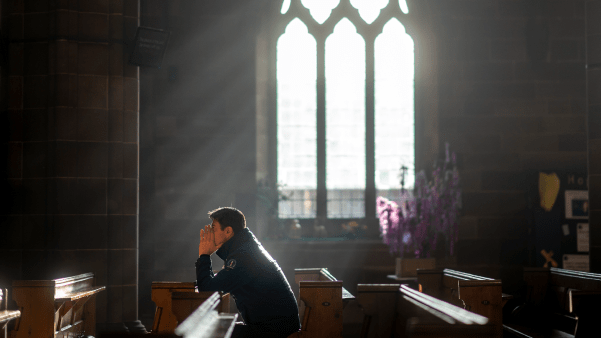 A man prays in a UK church amid bad news about the future of seminary education.