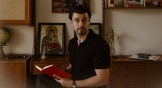 portrait of Josh Nadeau holding a notebook against a gallery wall and bookshelf.