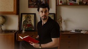portrait of Josh Nadeau holding a notebook against a gallery wall and bookshelf.
