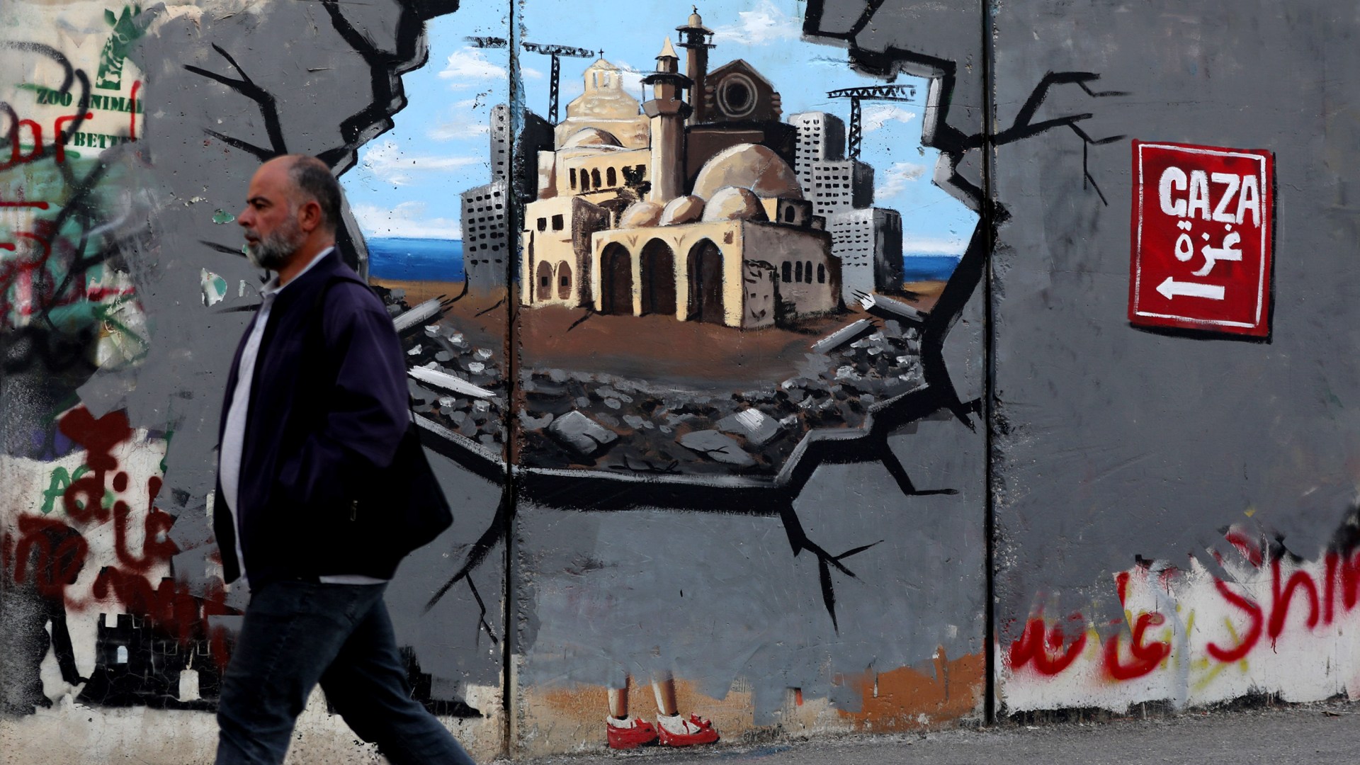 A man walks past graffiti on the Bethlehem side of the Separation Wall supporting the reconstruction of the Gaza Strip.