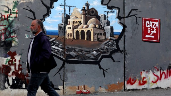 A man walks past graffiti on the Bethlehem side of the Separation Wall supporting the reconstruction of the Gaza Strip.