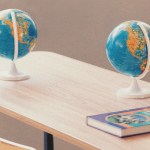 Two globes on a desk with an English text book on it
