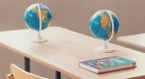 Two globes on a desk with an English text book on it