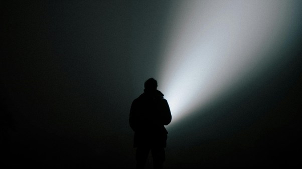 Man standing in the dark with a beam of light.