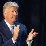 Robert Morris wears a navy suit and claps on stage.