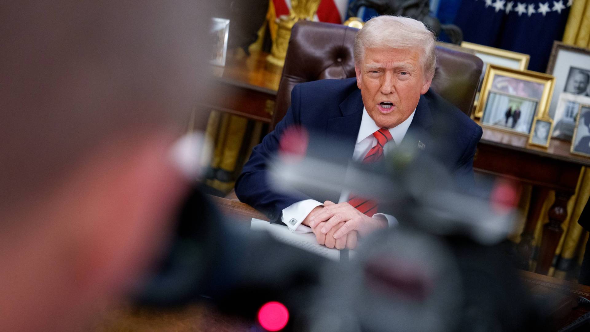 Donald Trump sitting at his desk in the Oval Office speaking to cameras