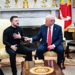 Zelensky and Trump, seated in front of flags, motion to each other while arguing during a meeting.