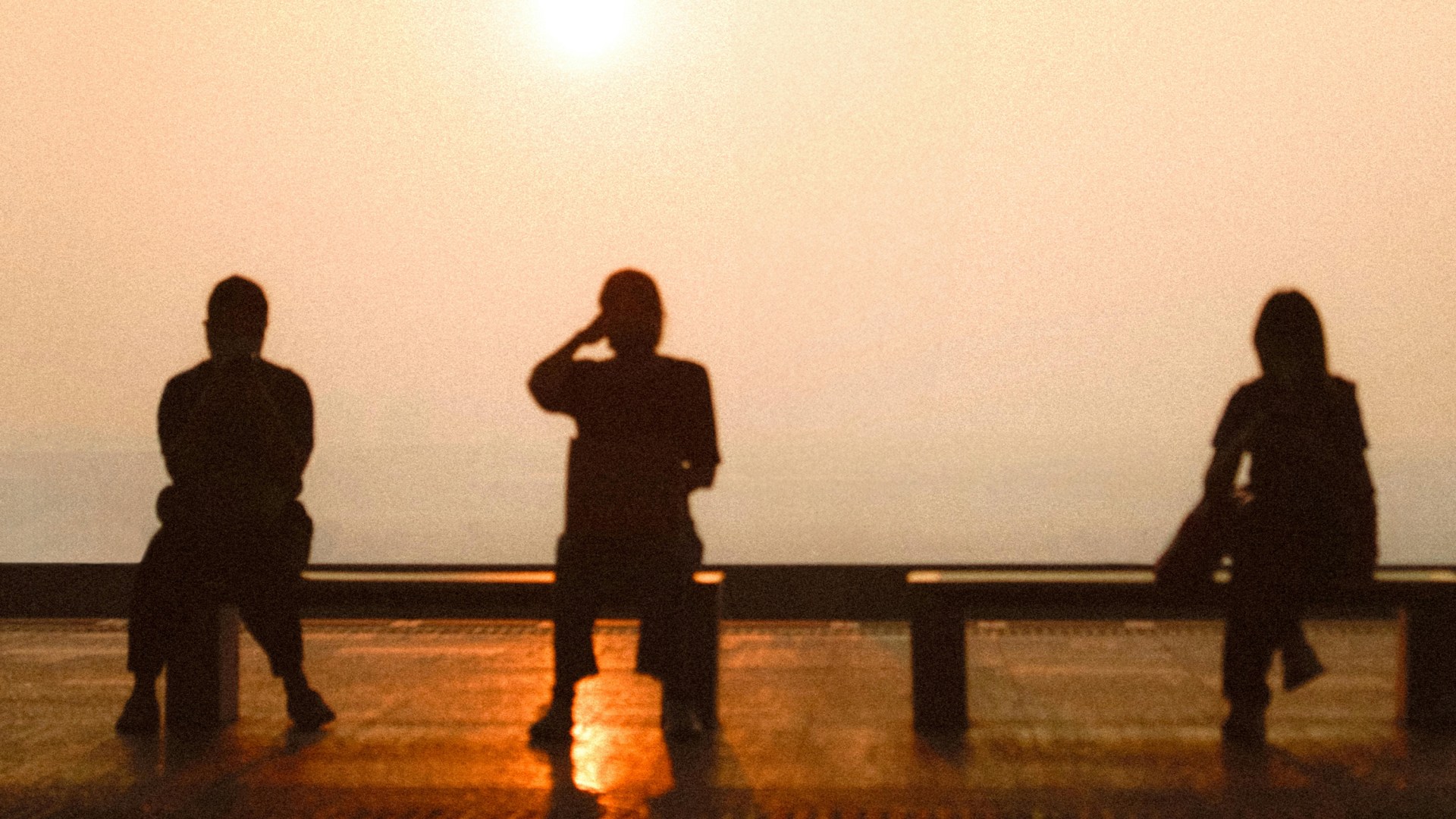 A photo of people sitting far apart on a bench.