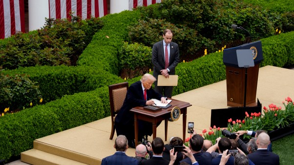 U.S. President Donald Trump, accompanied by White House staff secretary Will Scharf, signs an executive order imposing tariffs on imported goods.