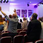 A man raises hands in rows of seats of people worshipping.