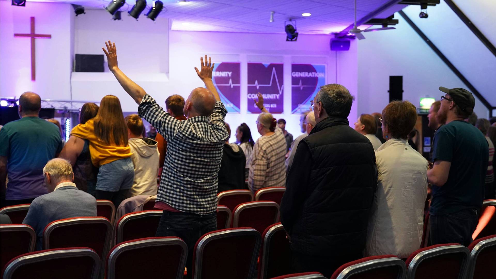 A man raises hands in rows of seats of people worshipping.