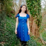 Nina Maksimova standing in a magical forrest wearing a blue dress.