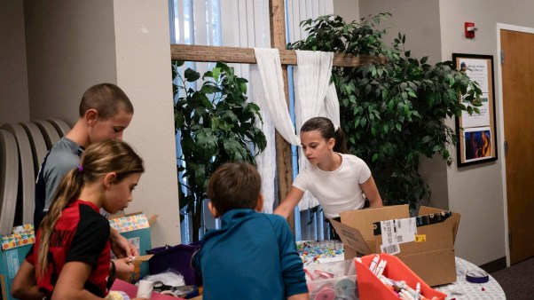 Students with school supplies in front of a cross