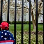Boy in MAGA hat and flag jacket stands outside White House gate