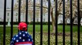 Boy in MAGA hat and flag jacket stands outside White House gate