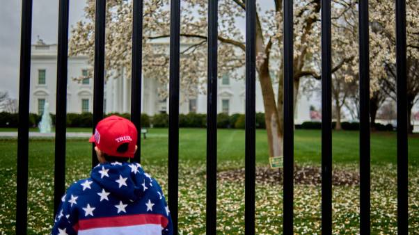 Boy in MAGA hat and flag jacket stands outside White House gate