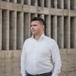 Lucian Mustata stands against a post-Communist architectural concrete building.